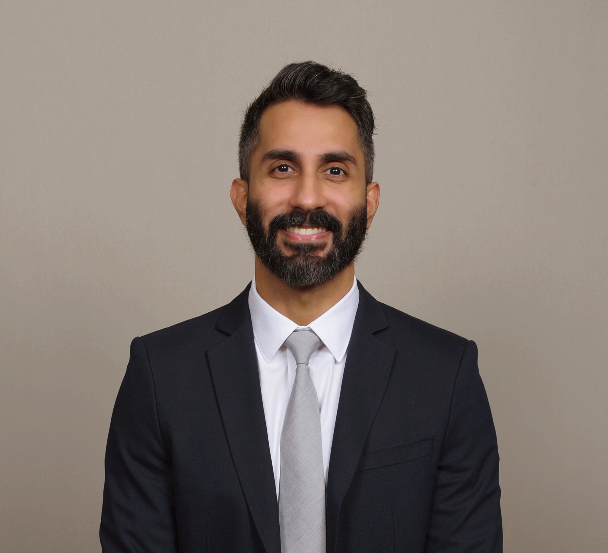 Professional headshot of a man in a dark suit and light tie, smiling against a neutral background.